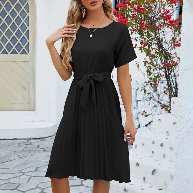 Woman wearing an elegant summer pleated dress with short sleeves and a flattering waist tie, ideal for warm-weather occasions.






