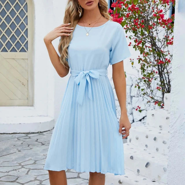 Woman wearing an elegant summer pleated dress with short sleeves and a flattering waist tie, ideal for warm-weather occasions.






